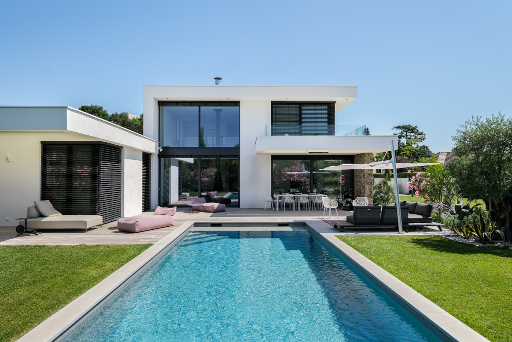 Maison moderne avec grandes baie vitrée qui donne sur une longue piscine d'un bleu azur