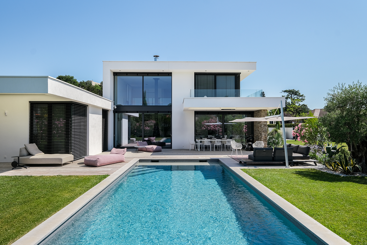 Maison moderne avec grandes baie vitrée qui donne sur une longue piscine d'un bleu azur
